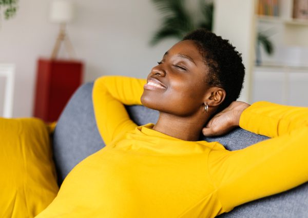 Young African American woman relaxing on a sofa at home - Smiling woman with hands behind head while relaxing on a couch at home.
